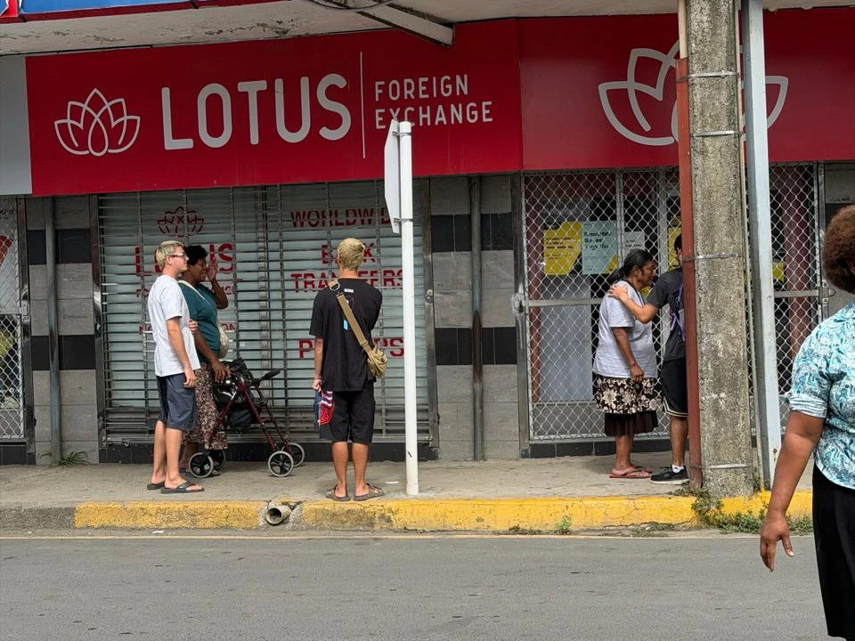A street scene in Fiji: the woman in a light gray top and dark patterned skirt receives prayer on the right; the team and her wheelchair are on the left.