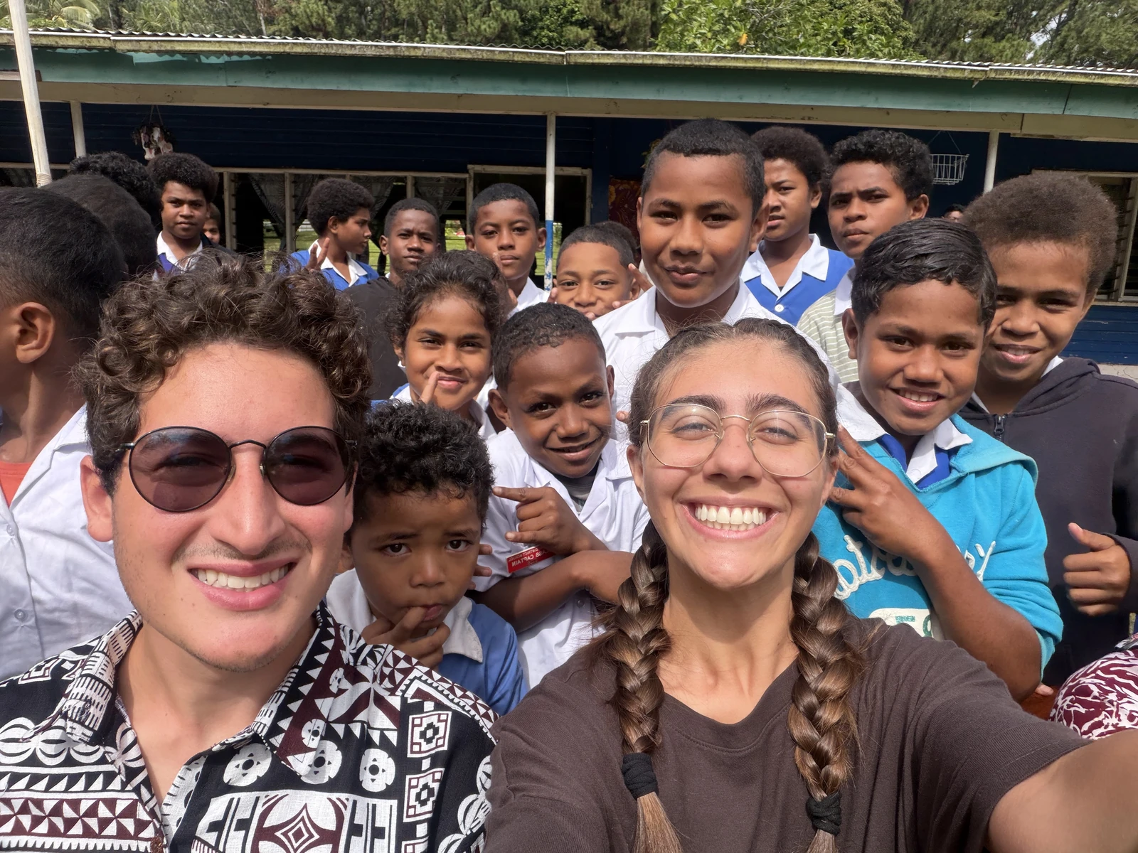 Gabriel and Rebecca smiling in a group photograph with students outside a school building.